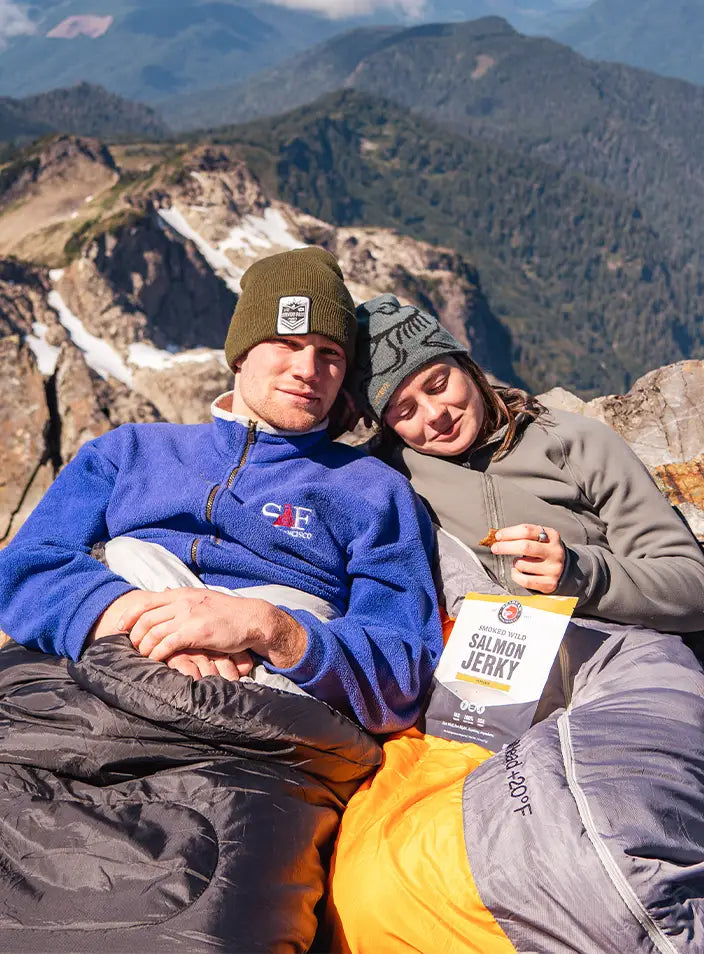 Two hikers on top of a mountain eating SeaBear's Peppered Smoked Wild King Salmon Jerky | SeaBear Smokehouse