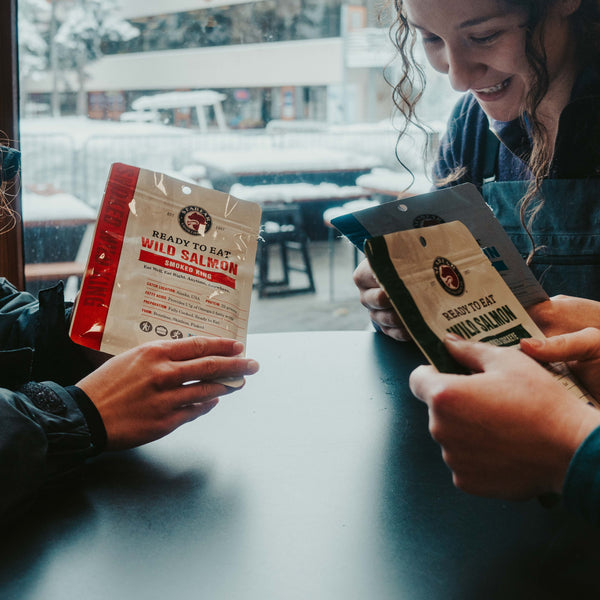 people sitting around a table holding pouches of SeaBear's Ready-To-Eat Sockeye Salmon Pouches | SeaBear Smokehouse