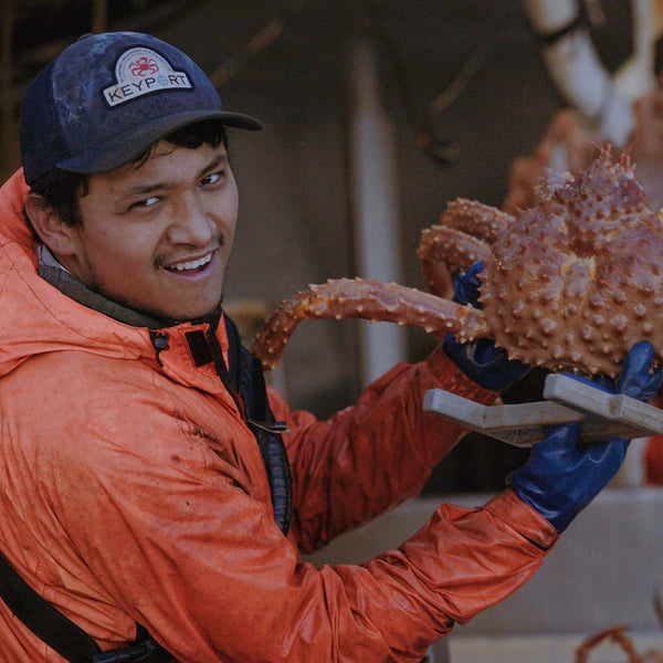 Keyport Crew Member Holding Crab with Hat | SeaBear Smokehouse | Keyport Crab